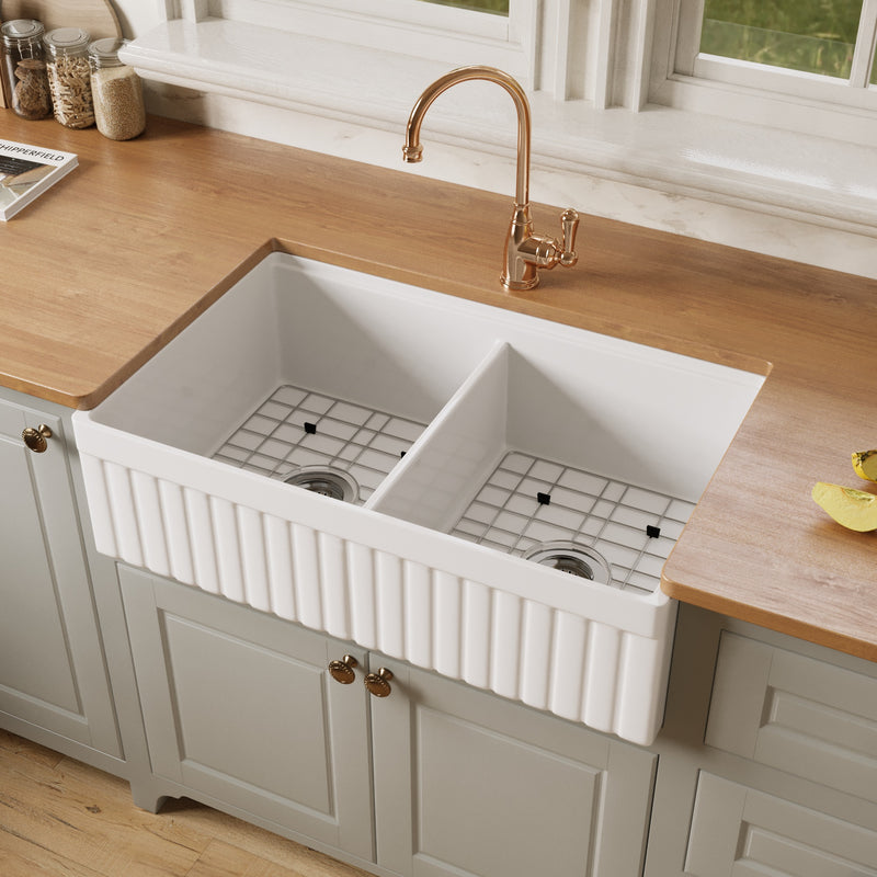 NOZLOO 33 inch double bowl fireclay farmhouse sink with bottom grids in both bowls, installed in a sage green kitchen with wood countertop