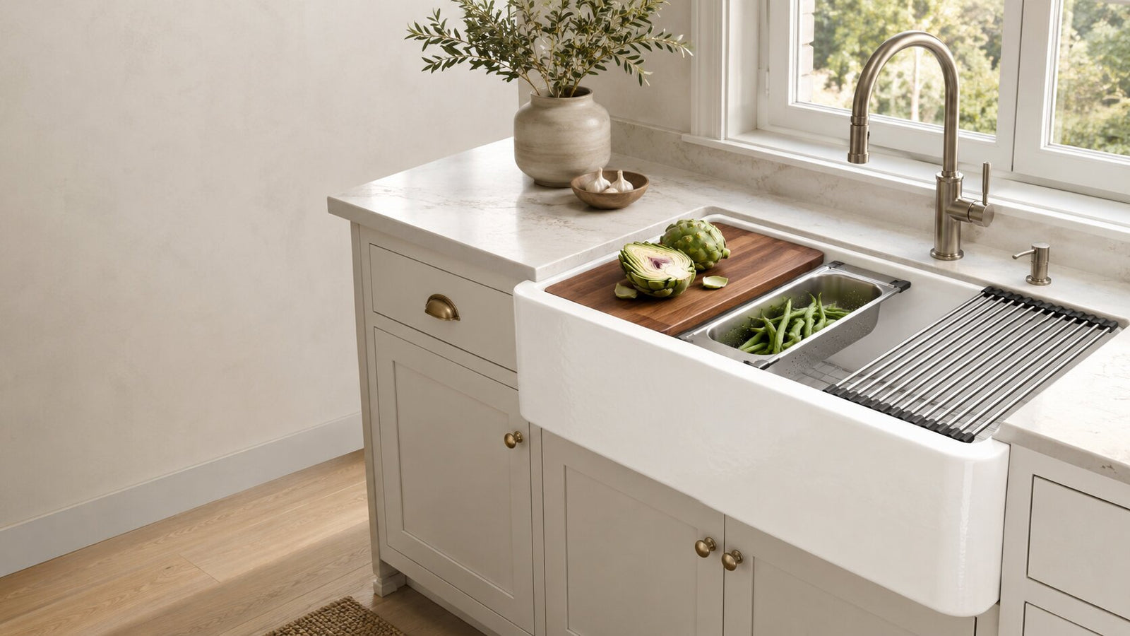 White fireclay workstation farmhouse sink with cutting board, colander, roll-up drying rack, and bottom grid in a bright modern kitchen.