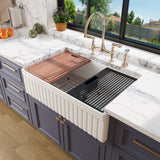 White 33 inch fluted fireclay farmhouse workstation sink with cutting board and roll-up drying rack in a blue kitchen with marble countertops