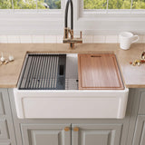 30 inch Grooved Apron Fireclay Farmhouse Sink with Workstation Kit featuring a cutting board, roll-up drying rack, bottom grid, and black colander tray on the integrated ledge