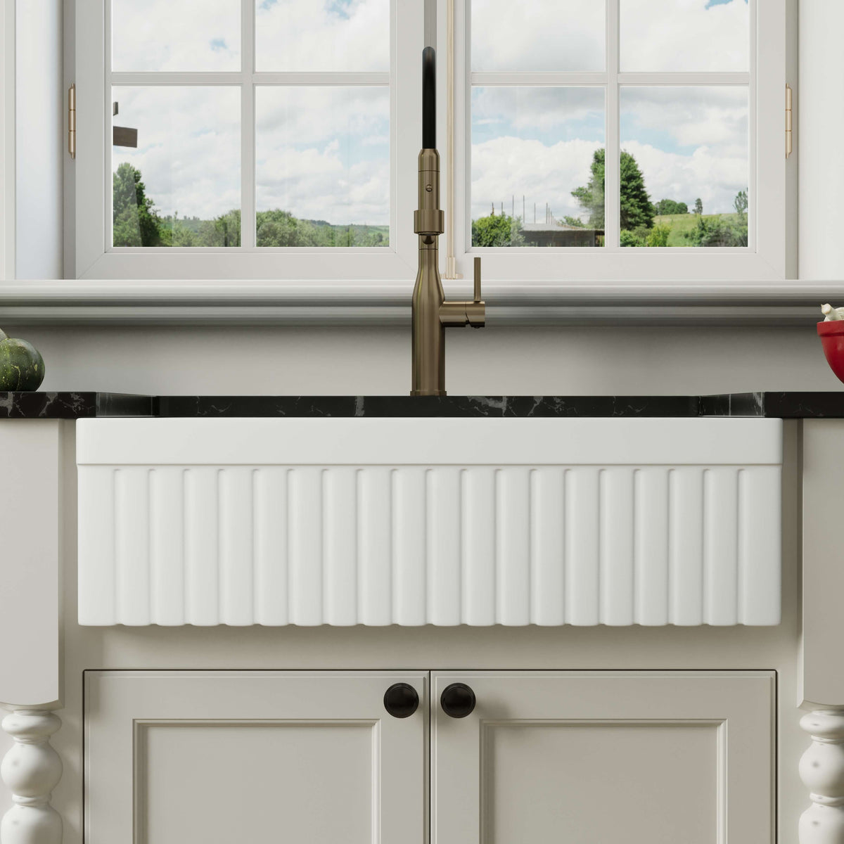 Front view of a white 33-inch reversible apron fireclay farmhouse sink installed beneath a brass faucet in a bright kitchen.