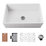 White reversible ribbed apron fireclay farmhouse sink with workstation accessories including cutting board, rack, grid, and drain