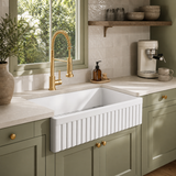 33 inch reversible apron fireclay farmhouse sink shown fluted-side-out in a sage green kitchen with brushed gold spring faucet and cream zellige tile